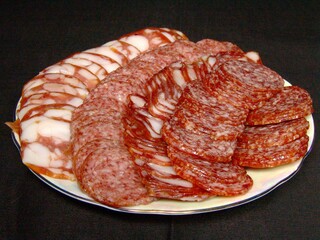 Slices of sausage and lard on a plate over solid background