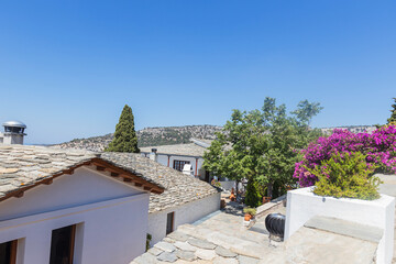 Fototapeta premium Peaceful monastery courtyard featuring blooming bougainvillea and traditional stone roofs in Thassos, Greece.