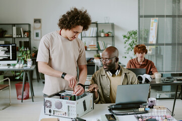 Biracial colleagues repairing old computer together in office of big IT company