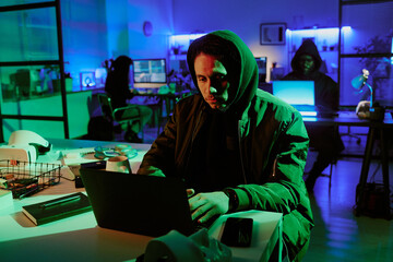 Medium close up of young man in black hoodie sitting at table and looking at laptop monitor tiredly