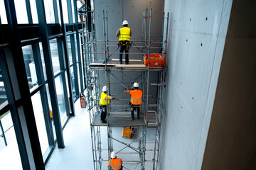 Workers on scaffolding performing construction tasks in a modern building, wearing safety gear for protection.