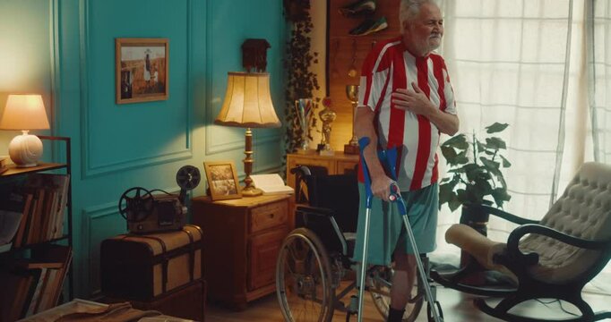 Old former soccer player senior man in red and white jersey with an amputated leg stands on one leg in front of a wheelchair and proudly sings the national anthem remembering moments from his youth.