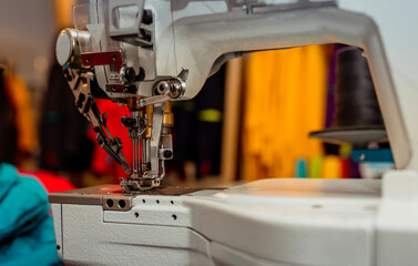 Close-up view of an industrial sewing machine with colorful fabrics and threads in the background. Perfect for themes related to fashion production, tailoring, and textile industry.