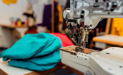 Close-up of an industrial sewing machine with colorful fabric in a workshop setting. Perfect for tailoring, textile industry, or handmade fashion themes.