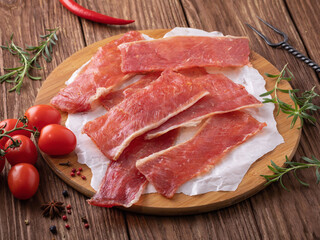 Raw smoked pork chips on a wooden tray with vegetables on the table, fresh snack for beer