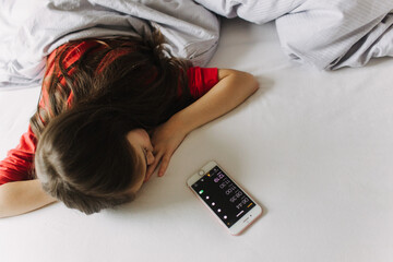 Pretty teenage girl lying under covers on bed. Getting up early in the morning, the overslept...