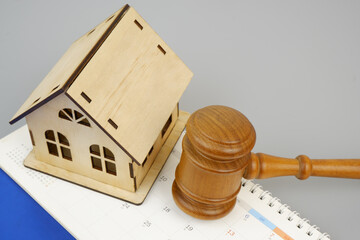 Wooden judge gavel and house model on calendar on gray background. Copy space for text.
