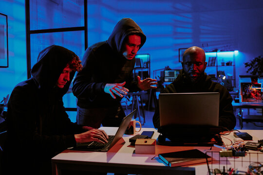 Biracial hackers dressed in black hoodies discussing programming details in office