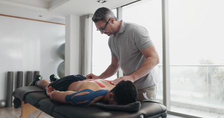 Physiotherapist, person and tape on bed for recovery process from injury, back pain and help at...