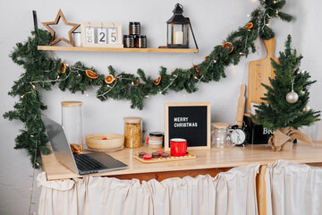 wooden kitchen with letterboard, open laptop and cup of coffee, decorated with Christmas decorations. Beautiful and cozy kitchen at Christmas