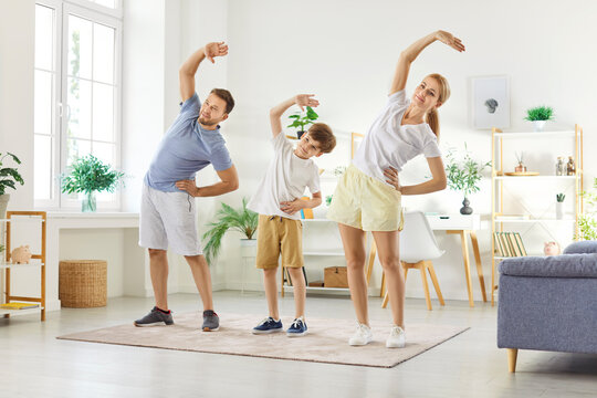 Sporty happy active young family doing morning sport training side bend exercises together in modern living room interior, smiling working out, pilates training, warming up in sportswear at home