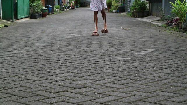 An Indonesian girl creatively uses a coconut shell as a stilt, showcasing traditional Indonesian games. A little girl balances on a coconut shell stilt, testing her limits. a symbol of childhood joy