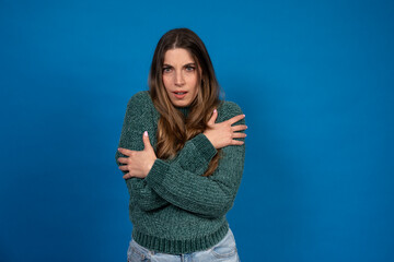 Freezing young woman rubbing her arms trying to get warm on blue background