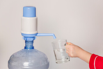 Woman's hand pouring water from a plastic bottle manual water pump dispensing into a glass on a white background