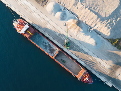 Sea freight, dry cargo ship bulk carrier is loaded with crushed stone in the port of Muuga on a summer evening, photo view from a drone.