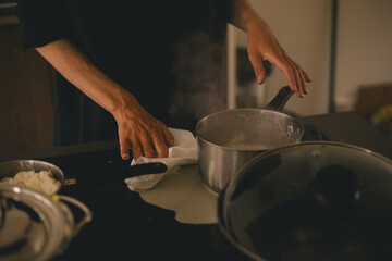 Dirty electrical stove after cooking, milk run out, woman wash stove with paper towel, hold pot pan with milk. Mess in kitchen.