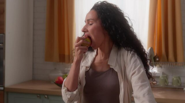 Hispanic woman Latina girl female lady Caucasian homeowner diet nutrition good habit throwing apple in air eating bite fruit smiling healthy food health care at home kitchen vitamin minerals eat happy