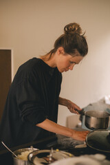 Dirty electrical stove after cooking, milk run out, woman wash stove with paper towel, hold pot pan with milk. Mess in kitchen.