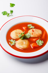Traditional Jewish tomato soup with matza balls, white background.