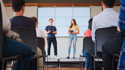 Two College Students Giving Presentation To High School Or University Class In Front Of Screen