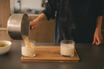 Matcha making process hand pouring milk in glass on wood desk in the kitchen.
