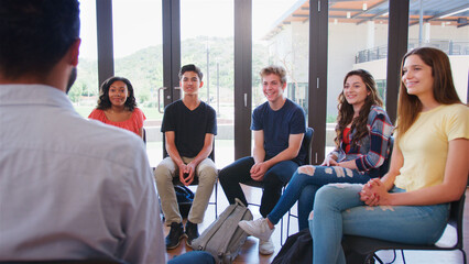 Male Tutor Teaching Group Of High School College Or University Students Sitting In Circle