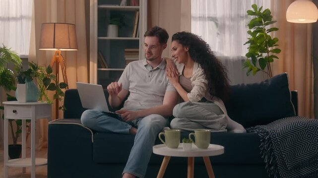 Smiling happy multiracial couple multiethnic Caucasian man male guy husband boyfriend with Hispanic Latina woman female girl wife girlfriend shopping computer together talking discuss laptop at home