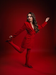 A beautiful young girl in a red jacket in red tights on a red background with a lush hairstyle and gold earrings on a red chair © Kiryl