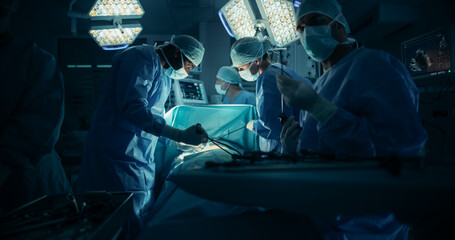 Skilled Male and Female Surgical Team Performing a Delicate Procedure in a Dimly Lit, Technological Hospital Room. Group of Healthcare Professionals Collaborating Around the Operating Table