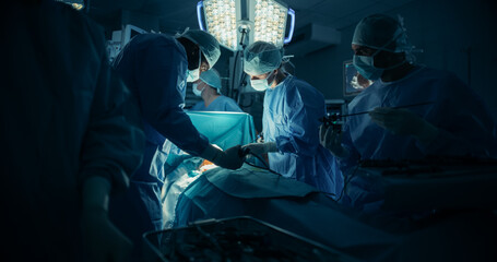 Diverse Surgical Team Working in a Darkened Operating Room Surrounded by Advanced Medical...