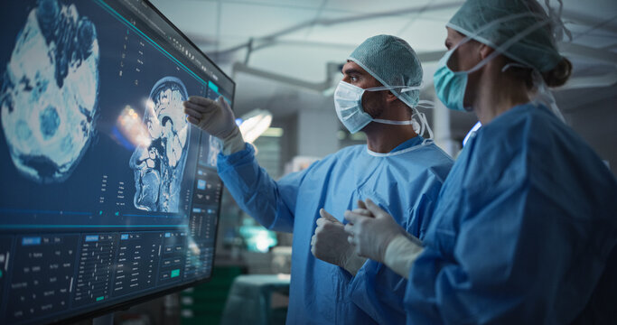 Caucasian Male and Female Surgeons Analyze Brain Scans on a Digital Monitor, Planning Surgical Strategy in a High-tech Operating Room. Colleagues Working Together, Preparing for Surgery