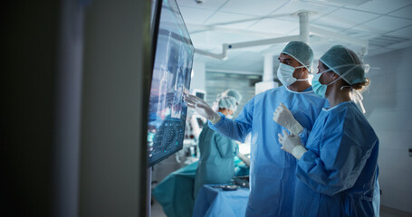 Caucasian Male and Female Surgeons Analyze Scans on a Digital Monitor, Planning Surgical Strategy...