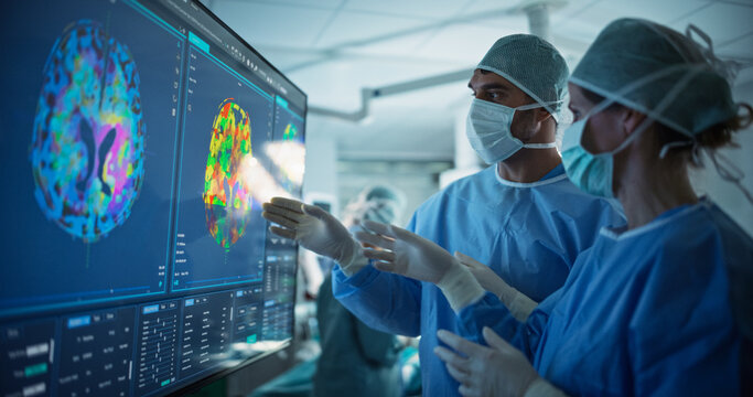 Before Beginning the Surgery, Female Lead Surgeon and an Assistant Looking at Detailed Brain PET Scans on a Large Computer Screen, Making Key Decisions Together with the Team