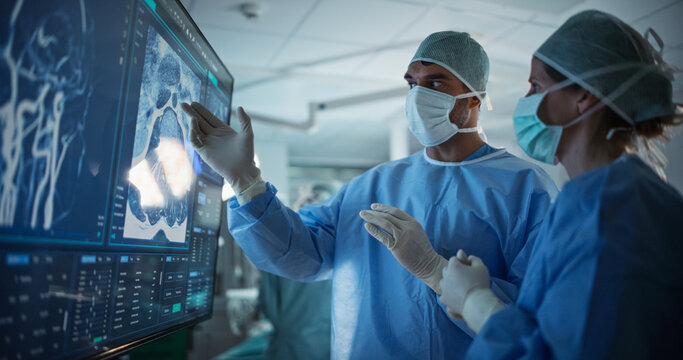 Portrait of a Young Female and Male Surgeons Reviewing Patient's Scans on a Large Screen in a Dimly Lit Operating Room. Their Team of Assistants and Nurses Preparing for a Life-Saving Procedure - Powered by Adobe