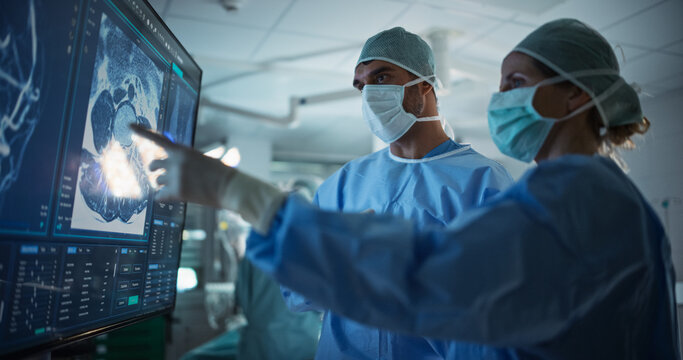 Caucasian Male and Female Surgeons Analyze Patient's Scans on a Digital Monitor, Planning Surgical Strategy in a High-tech Operating Room. Colleagues Working Together, Preparing for Surgery