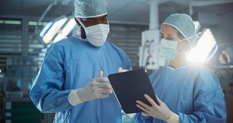Black Male and Caucasian Female Surgeons Analyze Information Online on a Tablet Computer, Planning...