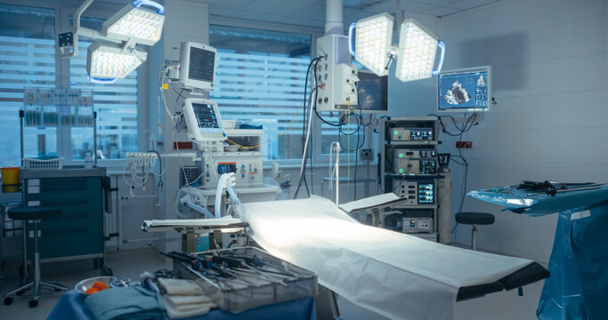 Empty Modern Hospital Operating Room Stands Ready with Computer Screens with Critical Medical Software, Precise Surgical Instruments and Arranged Tools in Sterile Clinical Setting