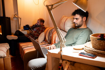 Father and son sitting on a large sofa working on a computer, looking at the mobile, disconnected from each other, in a warm and comfortable home working environment.