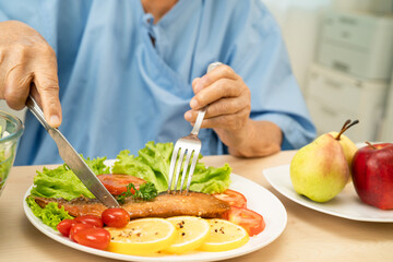 Asian elderly woman patient eating salmon stake and vegetable salad for healthy food in hospital.