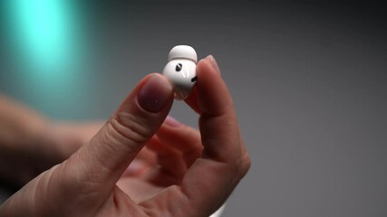 Close-up of unrecognizable woman with pink manicured nails holding new white wireless earbuds in hand, showcasing modern audio technology and sleek portable design for convenient listening experience.