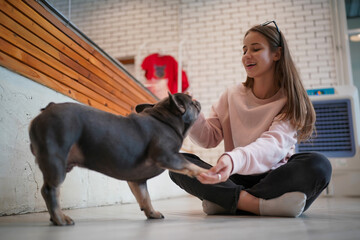 A smiling woman holding a cute black French Bulldog puppy while sitting