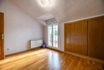 A bedroom in an attic room with custom-made wooden built-in wardrobes and a window leading out to a terrace