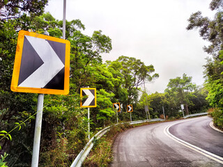 Curved road with warning signs indicating right turn in a lush green landscape on a cloudy day