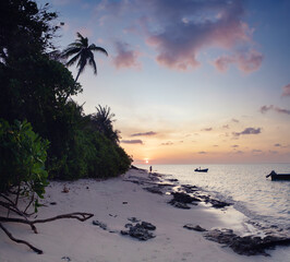 Beach sunset landscape with sun on horizon, purple and pink clouds in sky. Peaceful tropical paradise with incredible atmosphere of dream island, waves and lonely silhouette of man in distance