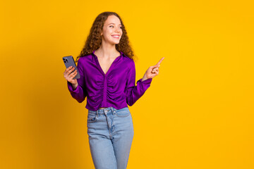 Photo of attractive young woman hold device point look empty space dressed stylish violet clothes isolated on yellow color background