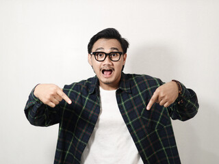 Smiling young handsome Asian man wearing a plaid shirt pointing fingers down, showing free place for advertisement isolated on white background. People lifestyle concept