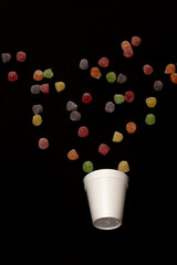 Scattered gummy candies on a black background with a foam cup at the bottom corner. Perfect for candy campaigns, creative projects, and themes of fun and childhood.