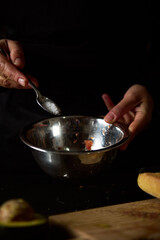 Hand adding salt to metal bowl during cooking preparation in dim lighting