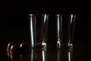 Two empty glasses and chocolates on a dark reflective surface