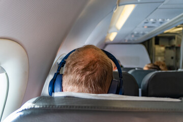 passenger seat, Interior of airplane with passengers sitting on seats and man listening to music....